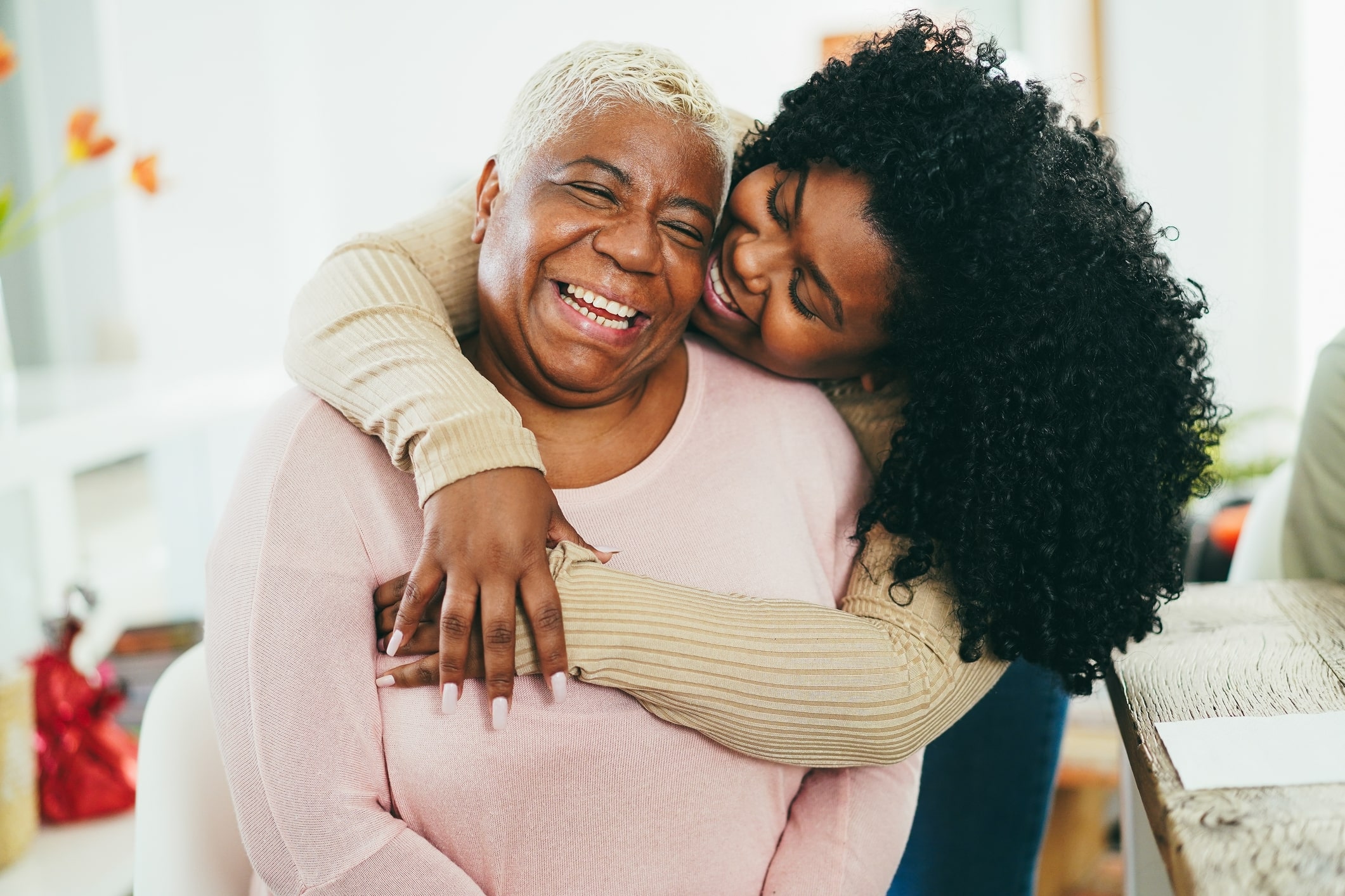 A young African daughter hugging her mom indoors at home - Main focus on senior mother face
