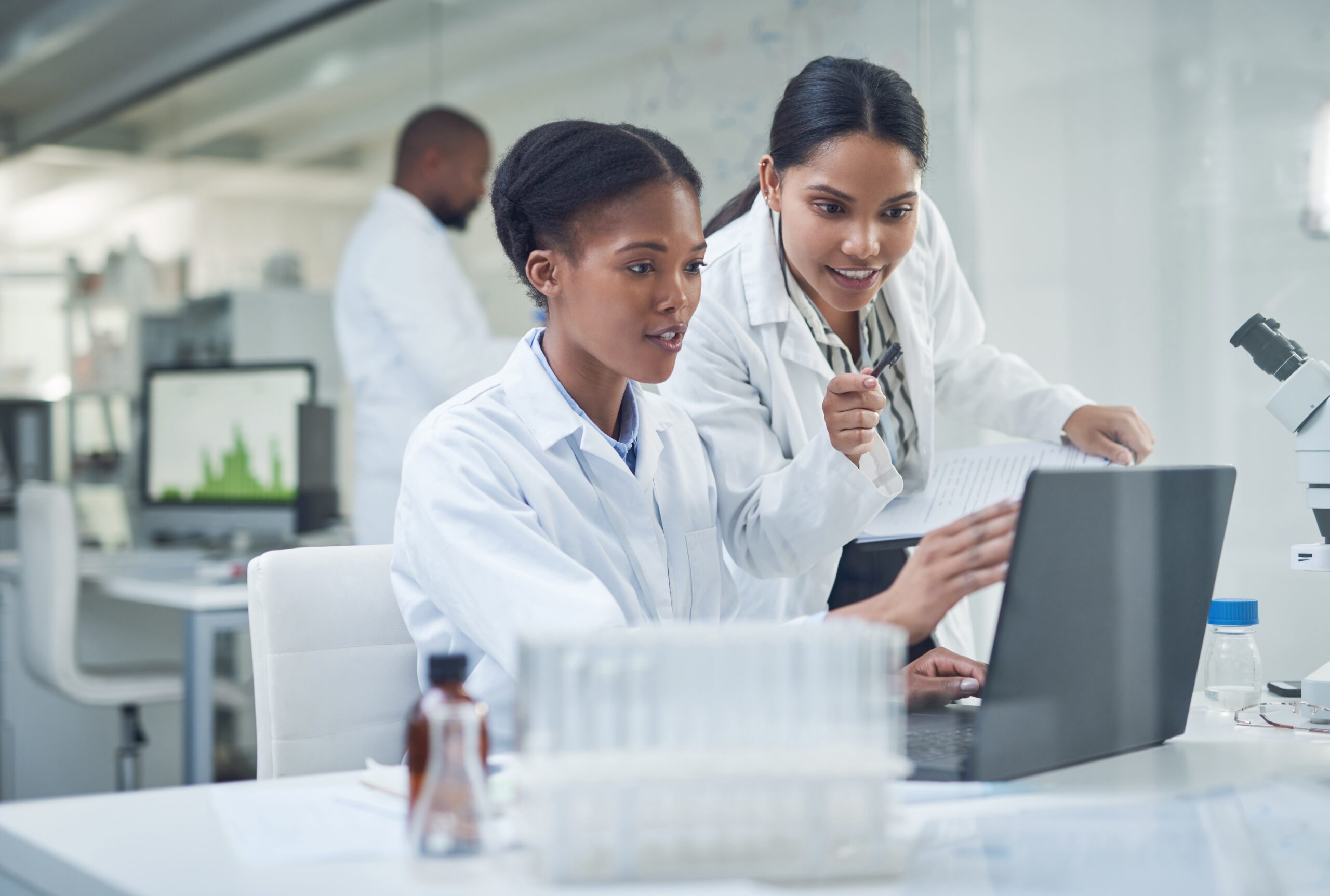 A young scientist shows another colleague something on her laptop in the laboratory.