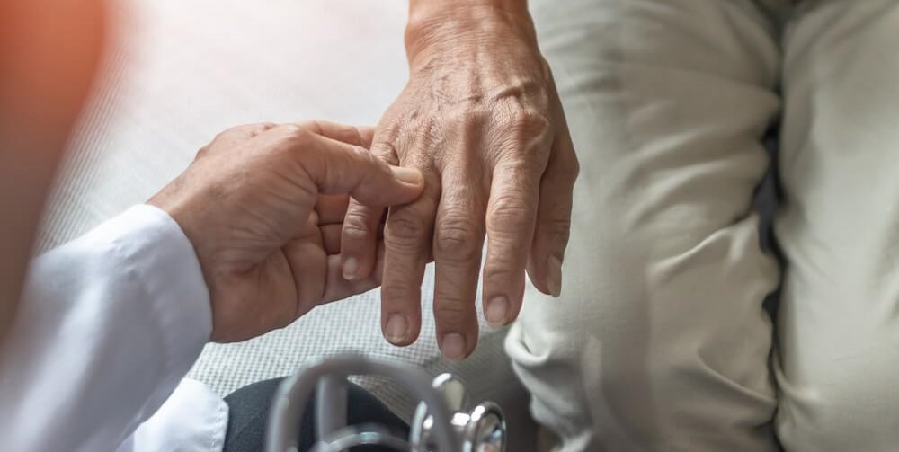 A closeup on a doctor grasping the hand of an older man.